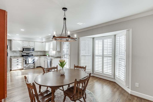 dining space featuring crown molding, baseboards, light wood-style floors, recessed lighting, and an inviting chandelier
