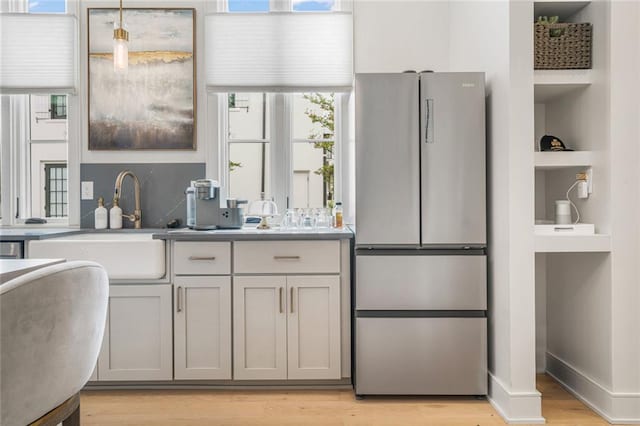 kitchen featuring a sink, light wood-style floors, light countertops, pendant lighting, and freestanding refrigerator