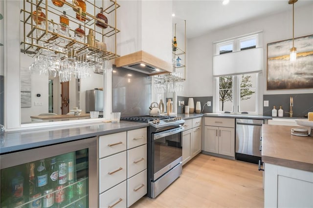 kitchen featuring decorative backsplash, light wood-type flooring, custom exhaust hood, appliances with stainless steel finishes, and beverage cooler