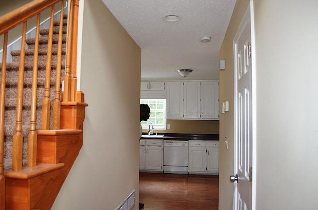 corridor with a textured ceiling, dark wood-type flooring, stairway, and a sink