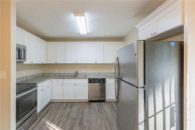 kitchen with white cabinets, stainless steel appliances, dark wood-type flooring, sink, and light stone counters