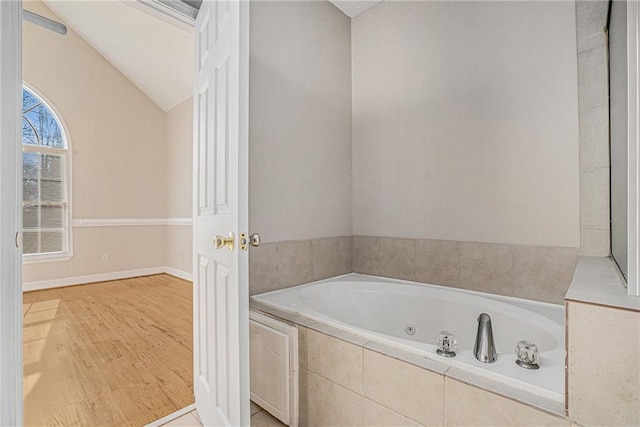 bathroom featuring lofted ceiling, hardwood / wood-style floors, and tiled bath