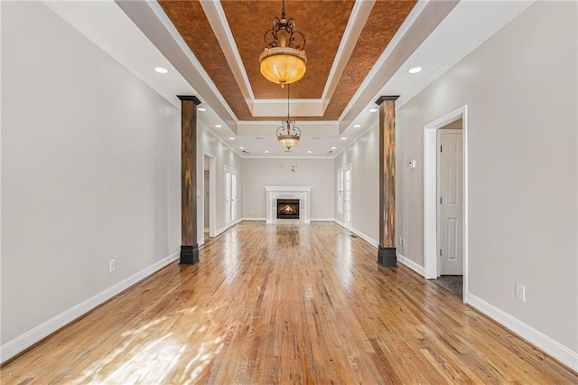 unfurnished living room with ornamental molding, light wood-type flooring, a raised ceiling, and a chandelier