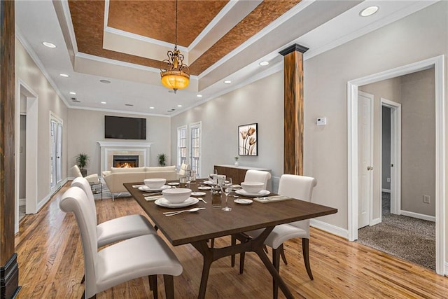 dining area featuring ornamental molding, light wood-type flooring, an inviting chandelier, and a raised ceiling