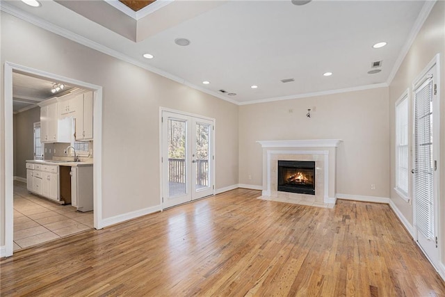 unfurnished living room featuring sink, french doors, ornamental molding, and light wood-type flooring