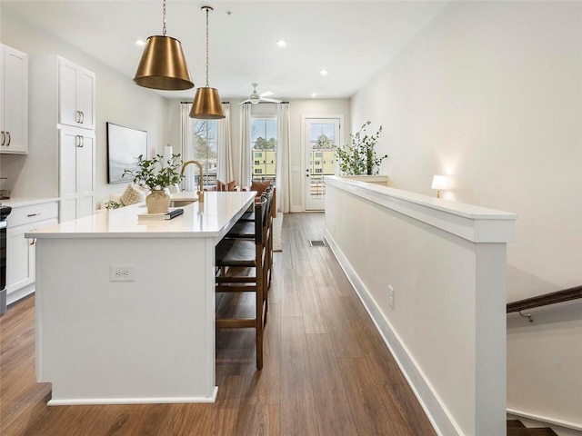 kitchen featuring a center island with sink, white cabinets, a breakfast bar, dark wood-style flooring, and light countertops