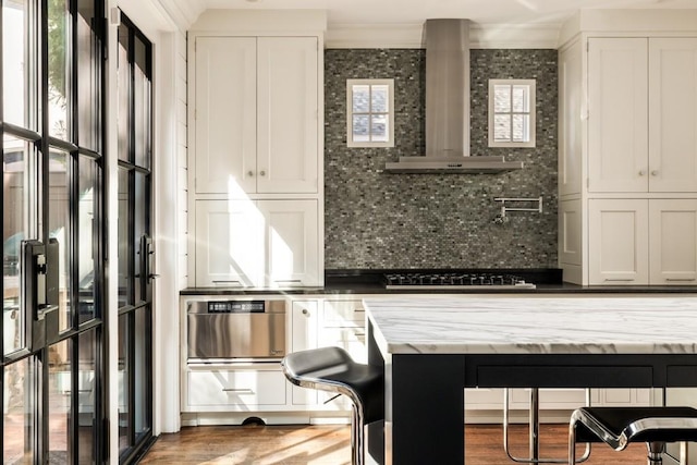 kitchen with white cabinetry, dark wood-type flooring, tasteful backsplash, ornamental molding, and wall chimney range hood