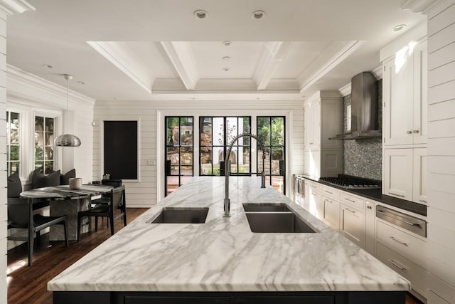 kitchen with an island with sink, stainless steel gas cooktop, light stone countertops, dark hardwood / wood-style floors, and wall chimney range hood