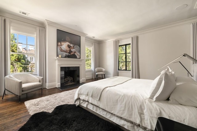 bedroom featuring multiple windows, dark hardwood / wood-style floors, ornamental molding, and a high end fireplace