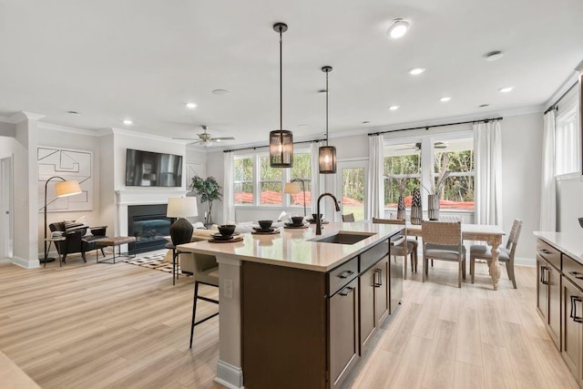 kitchen with ceiling fan, sink, decorative light fixtures, a center island with sink, and light hardwood / wood-style flooring