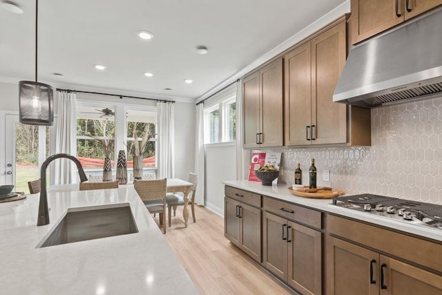 kitchen with stainless steel gas stovetop, sink, hanging light fixtures, light wood-type flooring, and tasteful backsplash