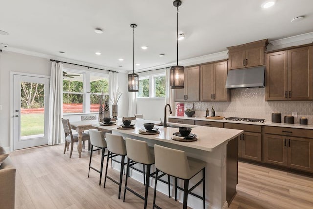 kitchen featuring pendant lighting, a kitchen island with sink, crown molding, sink, and stainless steel gas cooktop