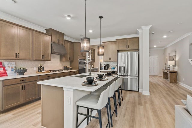 kitchen featuring appliances with stainless steel finishes, a breakfast bar, pendant lighting, light hardwood / wood-style flooring, and an island with sink