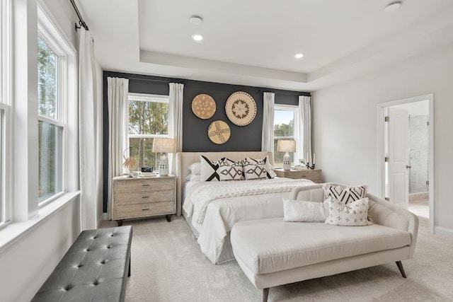 carpeted bedroom with a tray ceiling and ensuite bath