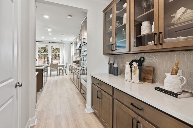 bar featuring light hardwood / wood-style floors, tasteful backsplash, ornamental molding, and stainless steel oven