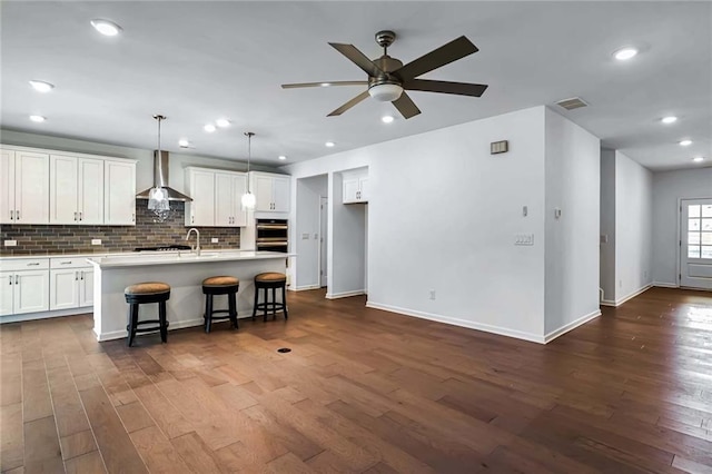 kitchen with a kitchen island with sink, wall chimney exhaust hood, pendant lighting, white cabinetry, and dark hardwood / wood-style flooring