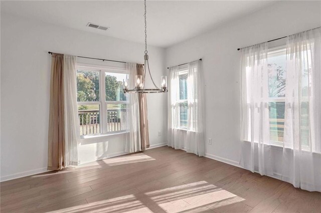 unfurnished dining area with an inviting chandelier and light hardwood / wood-style flooring