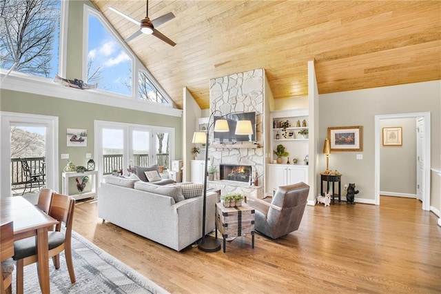 living area with high vaulted ceiling, a stone fireplace, wood ceiling, built in features, and light wood-style floors