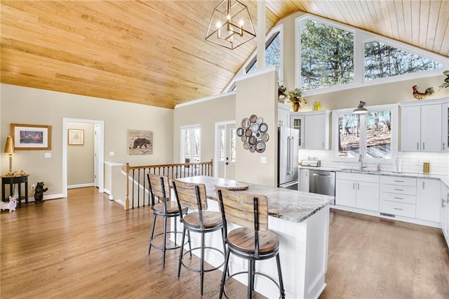 kitchen featuring light stone countertops, stainless steel appliances, a sink, wood ceiling, and decorative backsplash