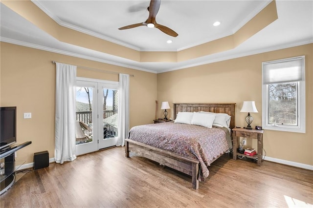 bedroom with a tray ceiling, access to outside, multiple windows, and wood finished floors