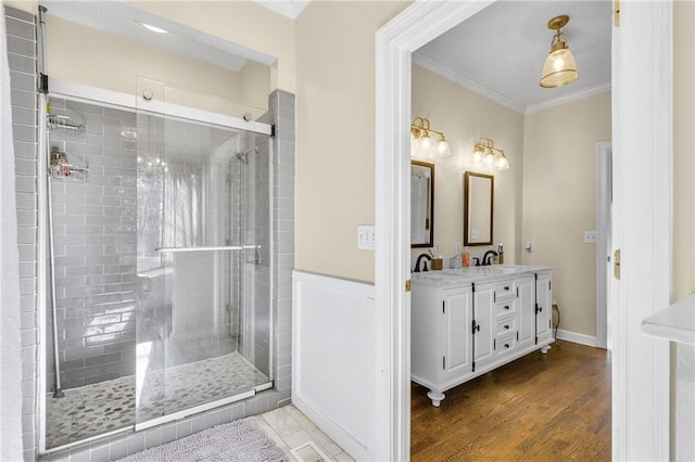 bathroom with double vanity, a shower stall, ornamental molding, and wood finished floors