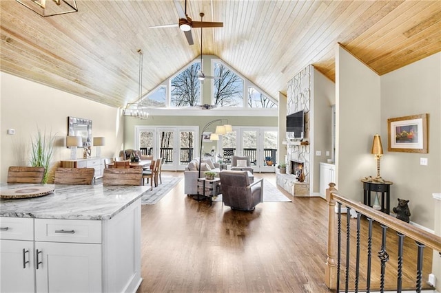 living room featuring wood ceiling, a stone fireplace, wood finished floors, high vaulted ceiling, and ceiling fan with notable chandelier