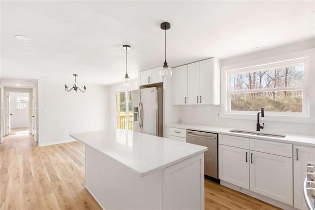 kitchen with white cabinets, appliances with stainless steel finishes, a center island, sink, and hanging light fixtures