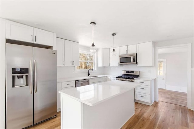 kitchen featuring white cabinets, a center island, decorative light fixtures, stainless steel appliances, and light wood-type flooring