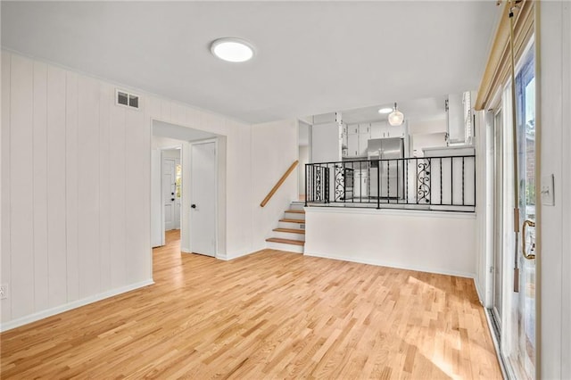 empty room featuring visible vents, light wood-style flooring, and stairs