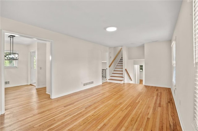 unfurnished living room featuring visible vents, light wood-style flooring, stairs, and an inviting chandelier