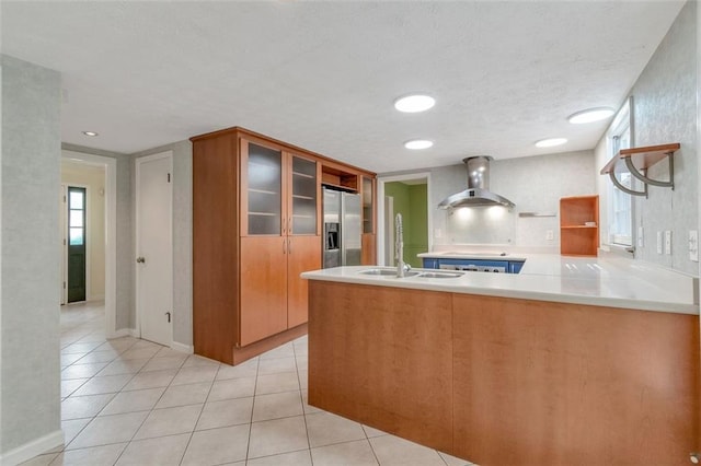 kitchen featuring light tile patterned floors, kitchen peninsula, sink, stainless steel fridge with ice dispenser, and wall chimney exhaust hood