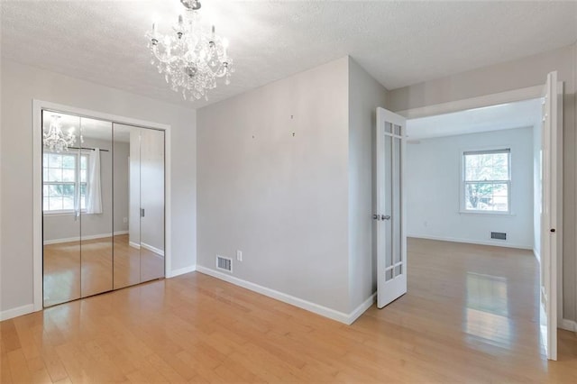 unfurnished bedroom featuring multiple windows, light hardwood / wood-style flooring, a notable chandelier, and a closet