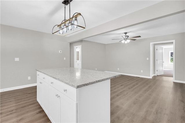 kitchen with wood finished floors, a center island, baseboards, white cabinets, and light stone countertops