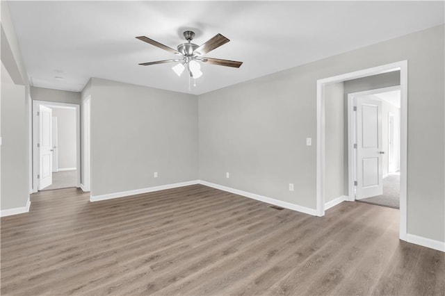 empty room with wood finished floors, visible vents, and baseboards