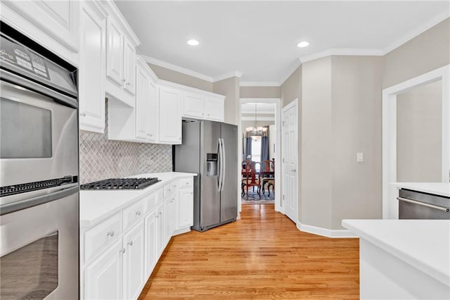 kitchen with appliances with stainless steel finishes, light wood-style flooring, light countertops, an inviting chandelier, and white cabinetry