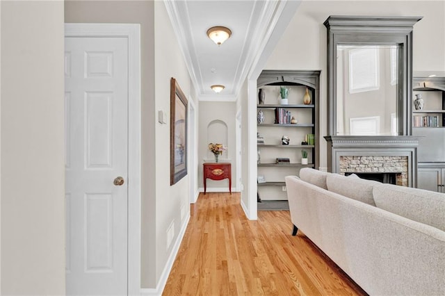 hallway featuring baseboards, ornamental molding, light wood-type flooring, and built in shelves