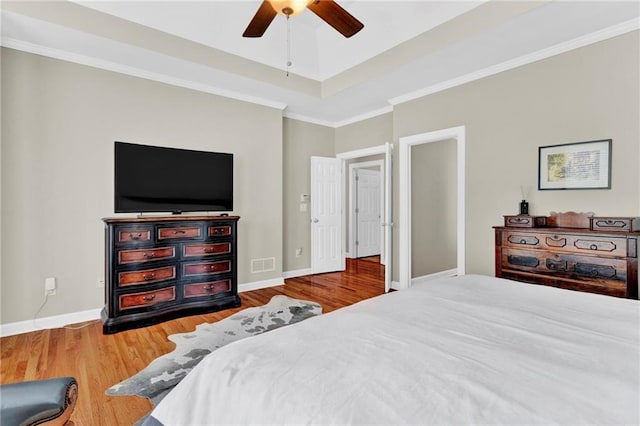 bedroom featuring a ceiling fan, baseboards, wood finished floors, visible vents, and ornamental molding