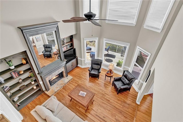 living room with a towering ceiling, a ceiling fan, a fireplace, and light wood-style floors
