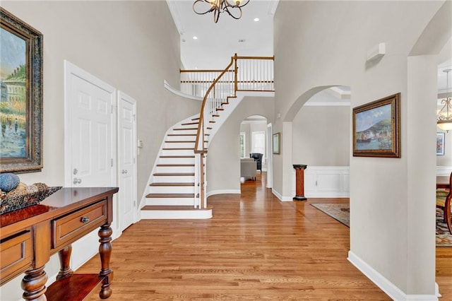 foyer entrance with arched walkways, a chandelier, a high ceiling, stairs, and light wood-style flooring