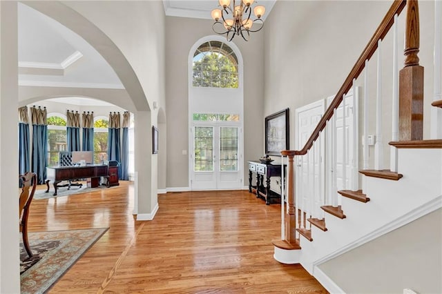 foyer featuring light wood-style floors, a towering ceiling, a notable chandelier, and stairway