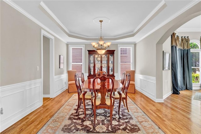 dining room featuring arched walkways, light wood-style flooring, a tray ceiling, and a notable chandelier