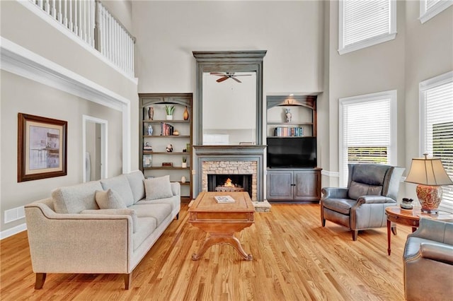 living area featuring ceiling fan, a stone fireplace, a towering ceiling, wood finished floors, and baseboards