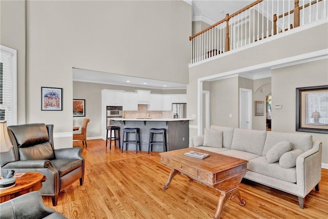 living area featuring a towering ceiling, crown molding, arched walkways, baseboards, and light wood finished floors