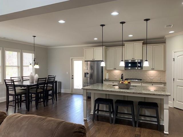 kitchen with light stone counters, a kitchen breakfast bar, an island with sink, pendant lighting, and stainless steel appliances