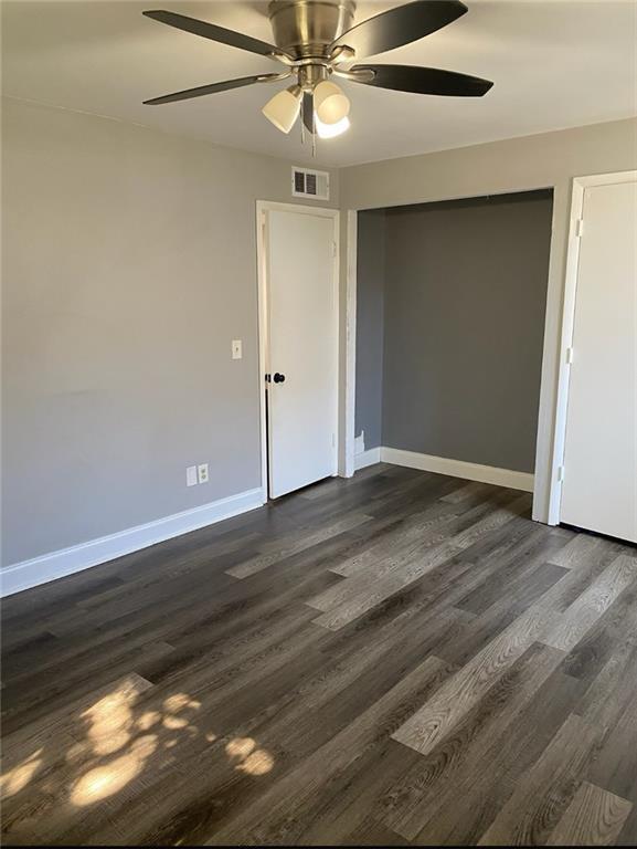 unfurnished room featuring visible vents, baseboards, dark wood-type flooring, and a ceiling fan