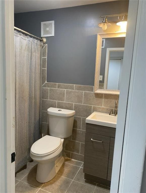 full bath featuring tile patterned flooring, a wainscoted wall, toilet, vanity, and tile walls