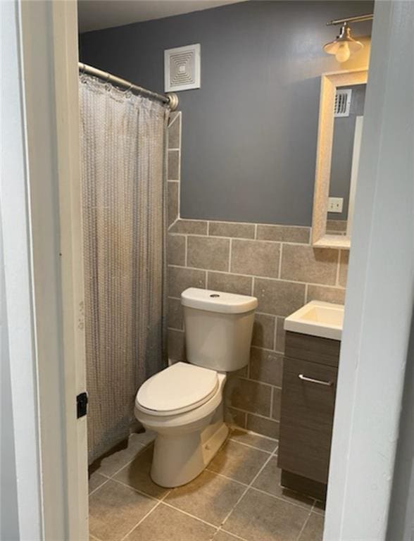 bathroom featuring tile patterned flooring, toilet, vanity, wainscoting, and tile walls