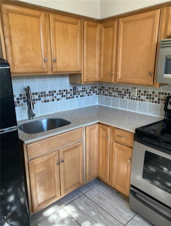 kitchen featuring electric stove, a sink, tasteful backsplash, freestanding refrigerator, and brown cabinetry