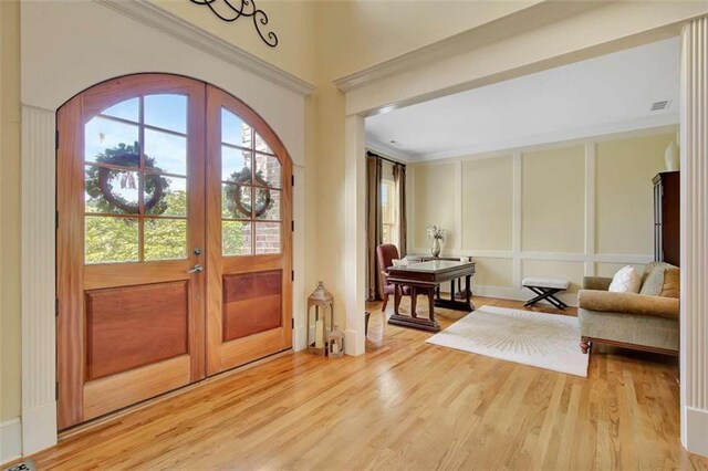 foyer entrance featuring french doors, light wood-type flooring, a decorative wall, and ornamental molding