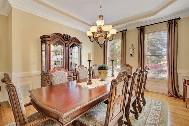 dining space with a chandelier, light wood-style floors, a wainscoted wall, and ornamental molding